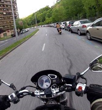 Una moto circula demasiado cerca de coches estacionados.