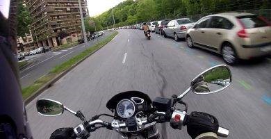 Una moto circula demasiado cerca de coches estacionados.