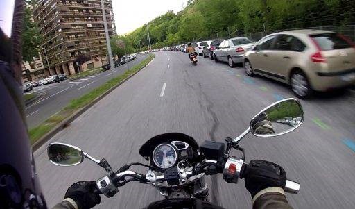 Una moto circula demasiado cerca de coches estacionados.