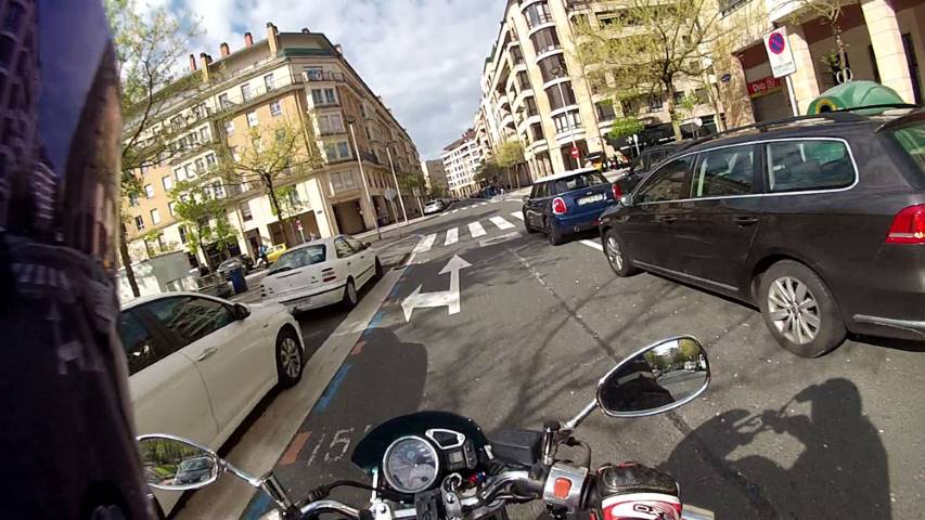 Una moto circula por una calle rodeada de coches estacionados
