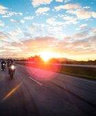 Varias motos circulan por una carretera con el sol a su espalda