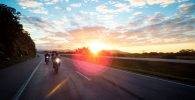 Varias motos circulan por una carretera con el sol a su espalda