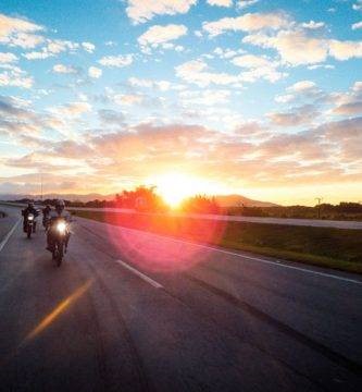 Varias motos circulan por una carretera con el sol a su espalda