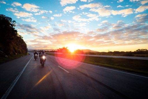 Varias motos circulan por una carretera con el sol a su espalda